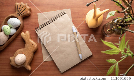 Blank notepad, pen, Easter figured wooden plates with eggs, spring twigs on wooden desk. Top view. 113091699