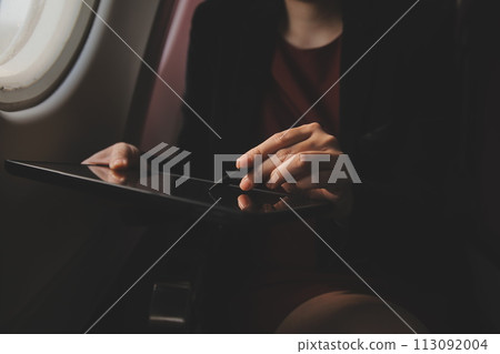 Blonde female tourist checking incoming notification on smartphone sitting on seat of airplane with netbook.Young businesswoman share media from telephone on laptop computer during plane flight Blonde female tourist checking incoming notification on smartphone sitting on seat of airplane with netbook.Young businesswoman share media from telephone on laptop computer during plane flight 113092004