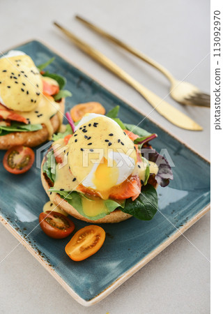 Eggs Benedict with salad leafs, salmon and fresh cherry tomato 113092970