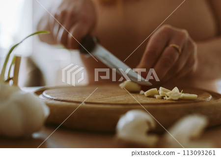 cooking, slicing garlic cloves on wooden cutting board cooking, slicing garlic cloves on wooden cutting board 113093261