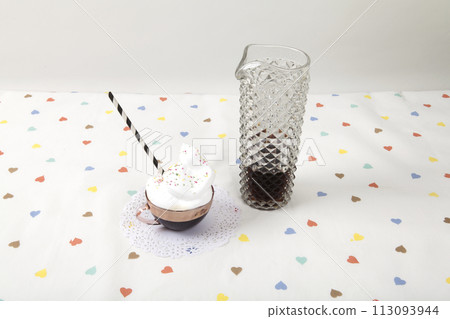 cup of coffee with whipped cream and sprinkles next to a vintage fake crystal decanter 113093944
