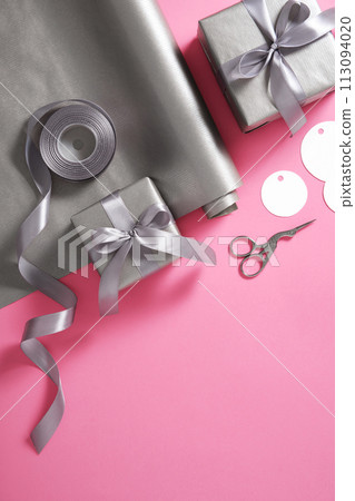Card with gift wrapping. Gray paper, silver ribbon, scissors on pink background. Vertical, place for text 113094020
