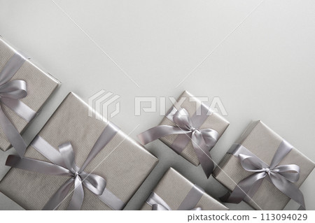 Monochrome gray gift boxes with gray ribbons on light background. Place for your text. 113094029
