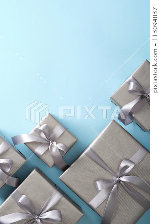 Gray gift boxes with silver ribbons on light blue background. Vertical, space for your text. 113094037