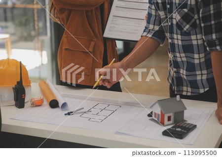 Male and Female Industrial Engineers in Hard Hats Discuss New Project while Using Laptop. They Make Showing Gestures.They Work in a Heavy Industry Manufacturing Factory. 113095500