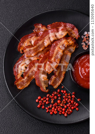 Delicious fresh fried bacon with salt and spices on a dark background Delicious fresh fried bacon with salt and spices on a dark background 113095640