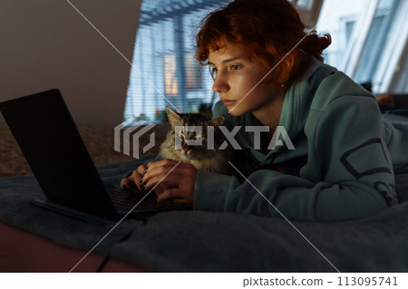 teenage girl spending time together with cat lying on bed using laptop 113095741