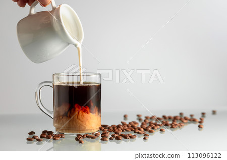 Pouring milk in black coffee. Pouring milk in black coffee. 113096122