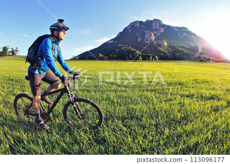 cyclist rides a bicycle on the green field towards the sun cyclist rides a bicycle on the green field towards the sun 113096177