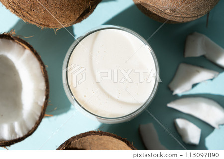 Coconut milk in a glass among coconuts on a blue background top view Coconut milk in a glass among coconuts on a blue background top view 113097090