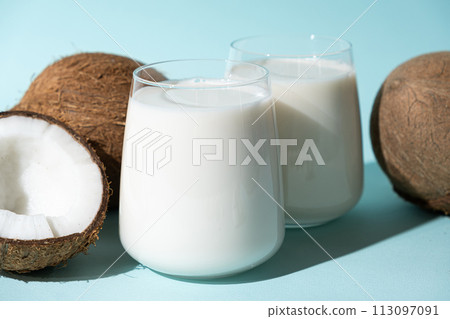 Coconut milk in a glasses among coconuts on a blue background 113097091