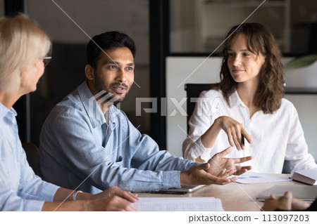 Positive motivated young Indian professional talking to group 113097203