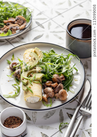 French rolled omelette stuffed with cream cheese with avocado, aragula and mushrooms for breakfast on white plate close up printed tile background 113099008