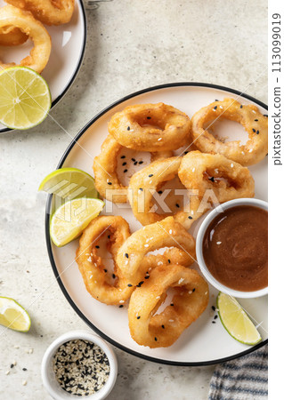 Crisp fried golden squid rings with lemon and sauce on a plate, light background , close up top view 113099019