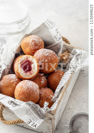 Cottage cheese donuts balls stuffed with jam with powdered sugar in wooden box. Healthy curd dessert. Selective focus 113099025
