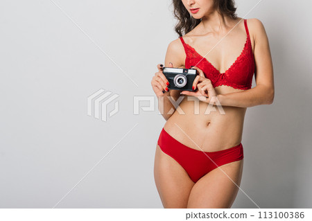 Beautiful female with pretty smile in red lingerie holding photo camera, isolated on white Beautiful female with pretty smile in red lingerie holding photo camera, isolated on white 113100386