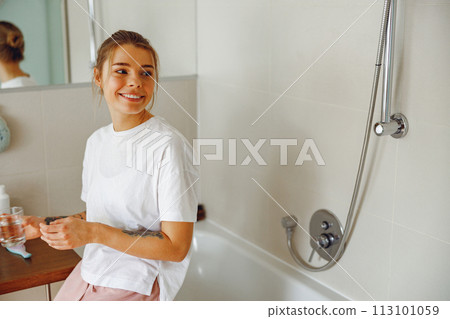 Positive young woman holding glass of water in the bathroom at home. Beauty treatment 113101059