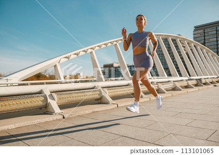 Young woman in sportswear is running on modern buildings background. Active lifestyle concept 113101065