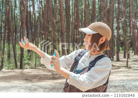 A woman using insect repellent spray and sunscreen spray at a campsite 113102848