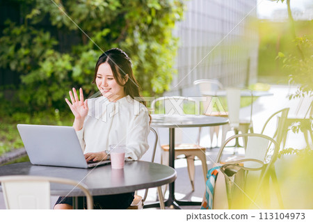 A business woman (nomadic worker) holding a web conference/video call on a computer on the terrace of a cafe A business woman (nomadic worker) holding a web conference/video call on a computer on the terrace of a cafe 113104973