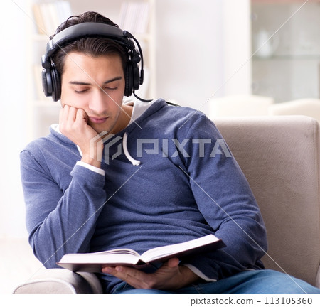 Young man reading book and listening to audio book Young man reading book and listening to audio book 113105360