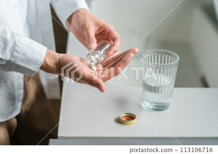 Hands of a sick man taking oral medicine, supplements, and medicines in the kitchen 113106716