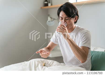 Sick man taking oral medicine, supplements, and pharmaceuticals in the bedroom / Medication 113106780