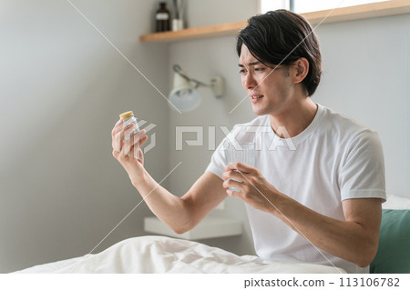 An unwell man looking at the ingredients of medicine in bed (cold, fever, headache, stomachache) 113106782