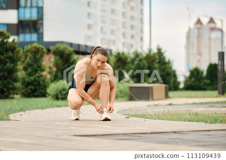 Woman tying the shoelaces on her way to sports ground. Woman tying the shoelaces on her way to sports ground. 113109439