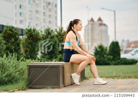 Woman bodybuilder resting while sitting on bench Woman bodybuilder resting while sitting on bench 113109443
