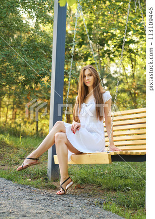 Young woman sitting on swing in city park 113109446