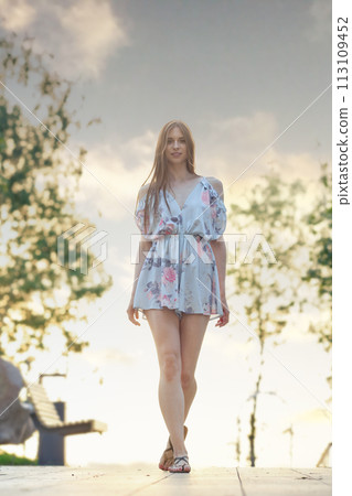 Young woman walking along park alley Young woman walking along park alley 113109452