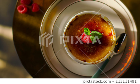 Creme brulee on the table decorated with raspberries and mint leaves, morning light from the windows, flat lay on popular desserts made from cream known as burnt cream or cream of the trinity 113111491