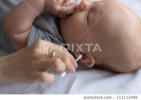 Female hand with wrong cotton swab near ear of a baby. Dangerous ears cleaning of the babies. 113112096