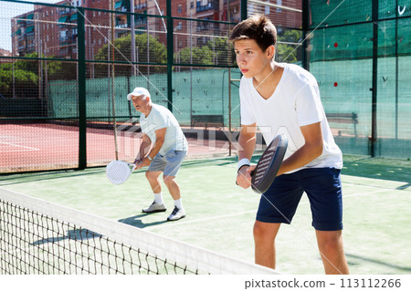 Mature man and young man playing padel court 113112266