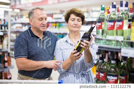 Mature couple husband and wife choose alcoholic drinks in supermarket Mature couple husband and wife choose alcoholic drinks in supermarket 113112276