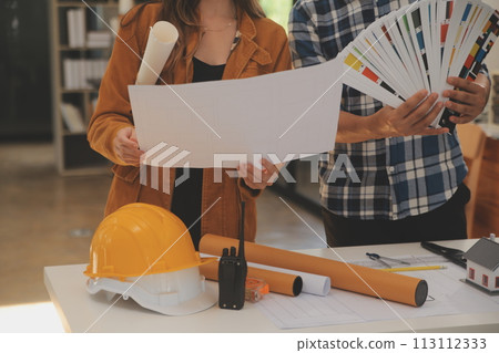 Male and Female Industrial Engineers in Hard Hats Discuss New Project while Using Laptop. They Make Showing Gestures.They Work in a Heavy Industry Manufacturing Factory. Male and Female Industrial Engineers in Hard Hats Discuss New Project while Using Laptop. They Make Showing Gestures.They Work in a Heavy Industry Manufacturing Factory. 113112333