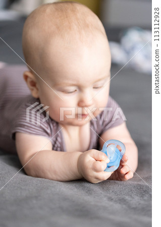Baby looking with interest to the blue pacifier. Baby looking with interest to the blue pacifier. 113112928