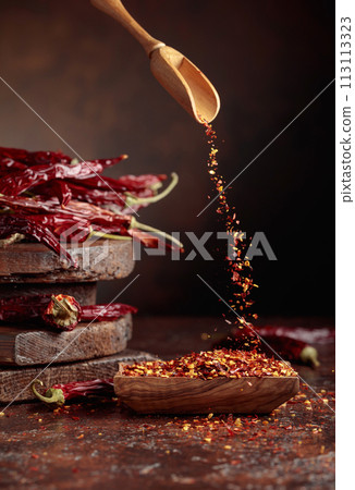 Chilli flakes are poured into a wooden dish. Chilli flakes are poured into a wooden dish. 113113323