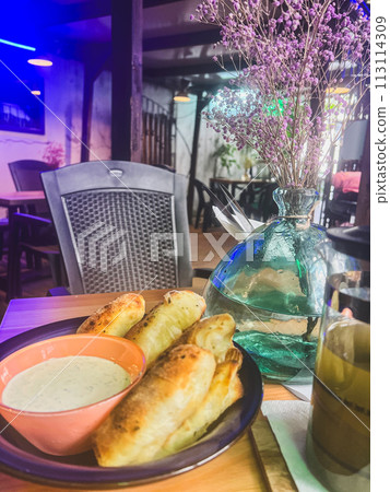 Breakfast in a cafe with a cup of coffee and pastries. Creamy sauce in a bowl and fried bread on the table 113114309