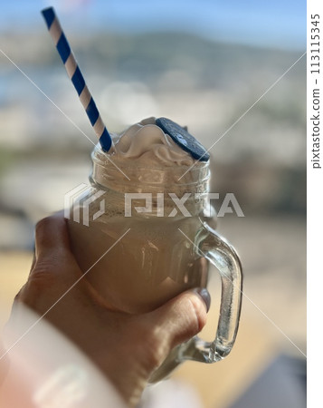 Iced coffee with whipped cream in a glass jar on the beach 113115345