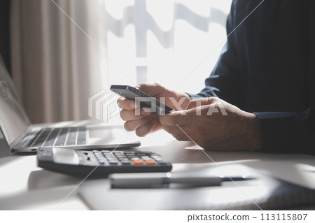 Side view shot of a man's hands using smart phone in interior, rear view of business man hands busy using cell phone at office desk, young male student typing on phone sitting at wooden table, flare Side view shot of a man's hands using smart phone in interior, rear view of business man hands busy using cell phone at office desk, young male student typing on phone sitting at wooden table, flare 113115807