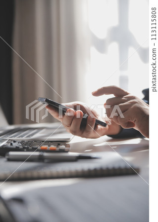 Side view shot of a man's hands using smart phone in interior, rear view of business man hands busy using cell phone at office desk, young male student typing on phone sitting at wooden table, flare Side view shot of a man's hands using smart phone in interior, rear view of business man hands busy using cell phone at office desk, young male student typing on phone sitting at wooden table, flare 113115808