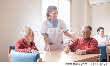 Happy nurse playing dominoes with senior people in nursing home 113116571