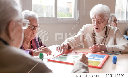 Senior woman playing ludo with friends at table in nursing home 113116591