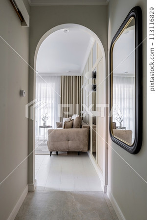 a hallway leading to a living room with a couch and a mirror a hallway leading to a living room with a couch and a mirror 113116829