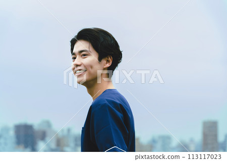 一位年輕的男性醫護人員微笑著，背景是一棟建築 113117023