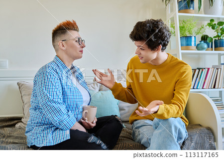 Happy middle-aged mother and son 19-20 years old, talking sitting together at home 113117165