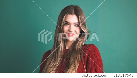 Pretty woman with long hair smiling in green studio 113117543