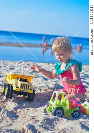 Happy toddler child playing on the beach with toy car 113121012